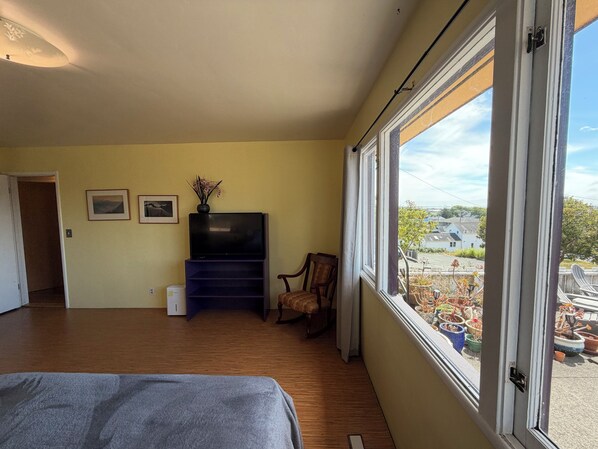 A bedroom with a bed, a TV on a stand, a chair, and a window with a view of the outside.