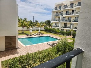 A pool area with lounge chairs, a wooden deck, and a view of a multi-story building with balconies. - Modern Studio in Central Park Downtown Punta Cana (Punta Cana)