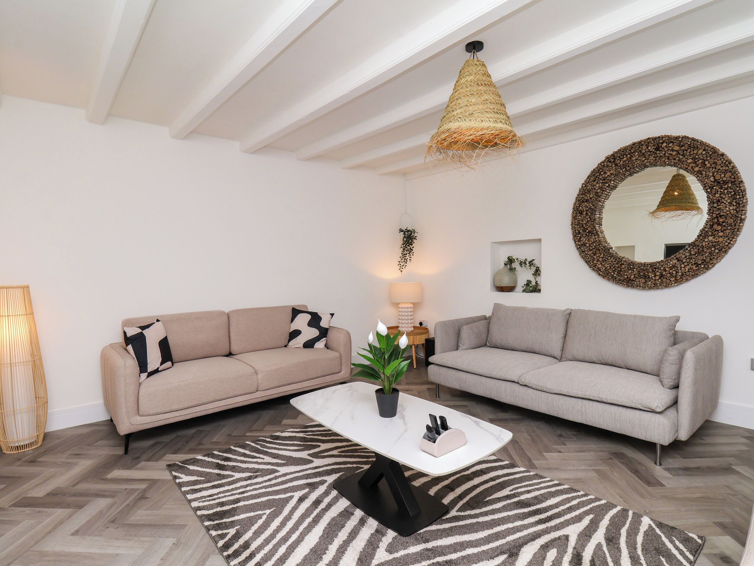 Una sala moderna con dos sofás, una mesa de centro, una lámpara colgante y un espejo decorativo.