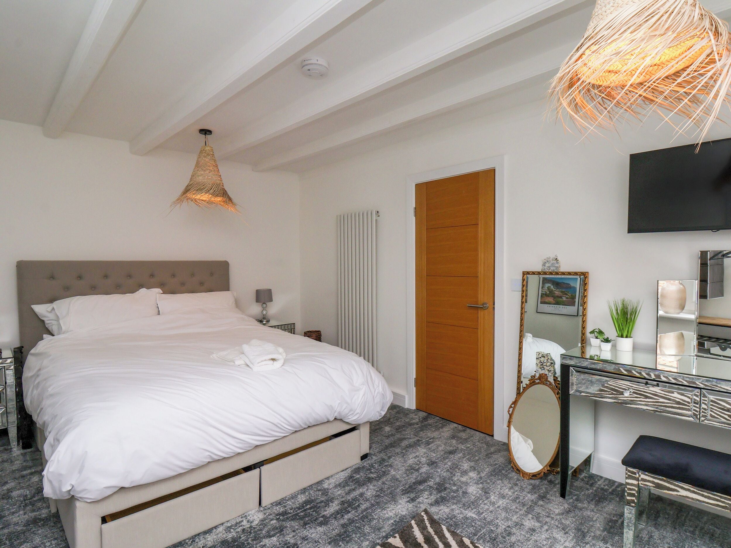 Une chambre d’hôtel avec un lit, une table de chevet, une lampe, un miroir et un téléviseur fixé au mur.