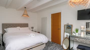 Habitación de hotel con cama, mesita de noche, lámpara, espejo y televisión en la pared.
