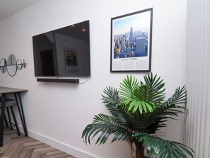 A modern room with a flat-screen TV mounted on the wall, a framed cityscape poster, and a potted plant. - Og's House (Whitby)