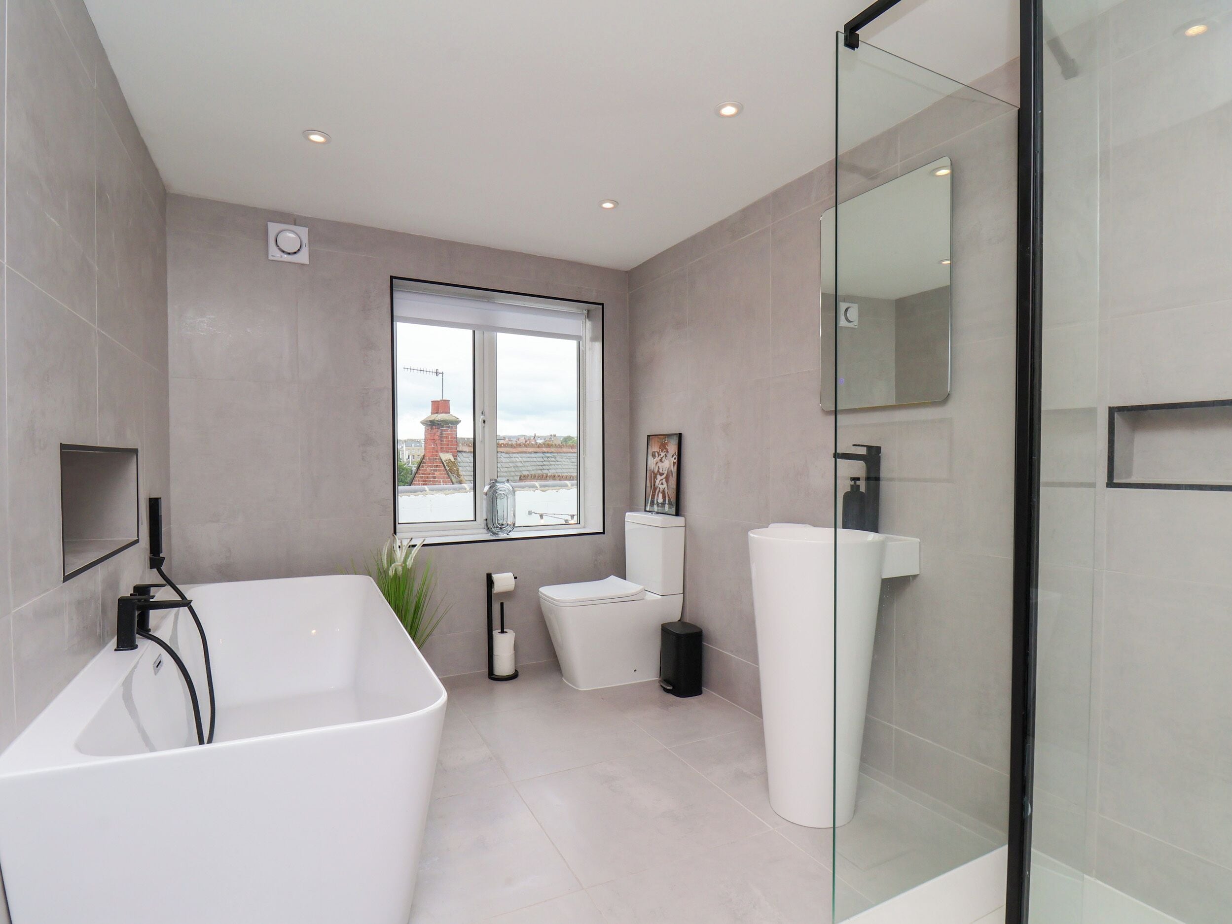 A modern bathroom with a large bathtub, a glass shower enclosure, and a large window providing a view of buildings outside.