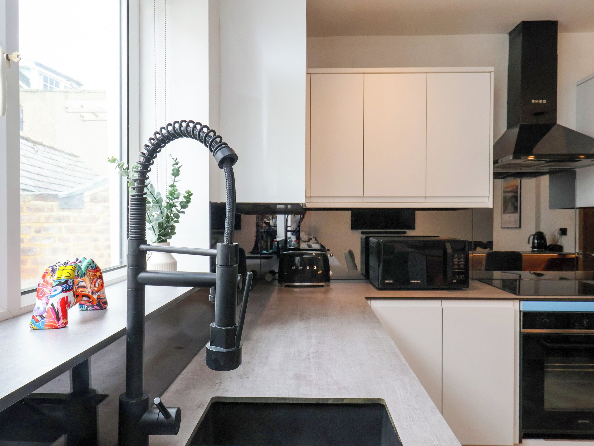 Una cocina moderna con armarios blancos, un microondas negro y un lavamanos de acero inoxidable.