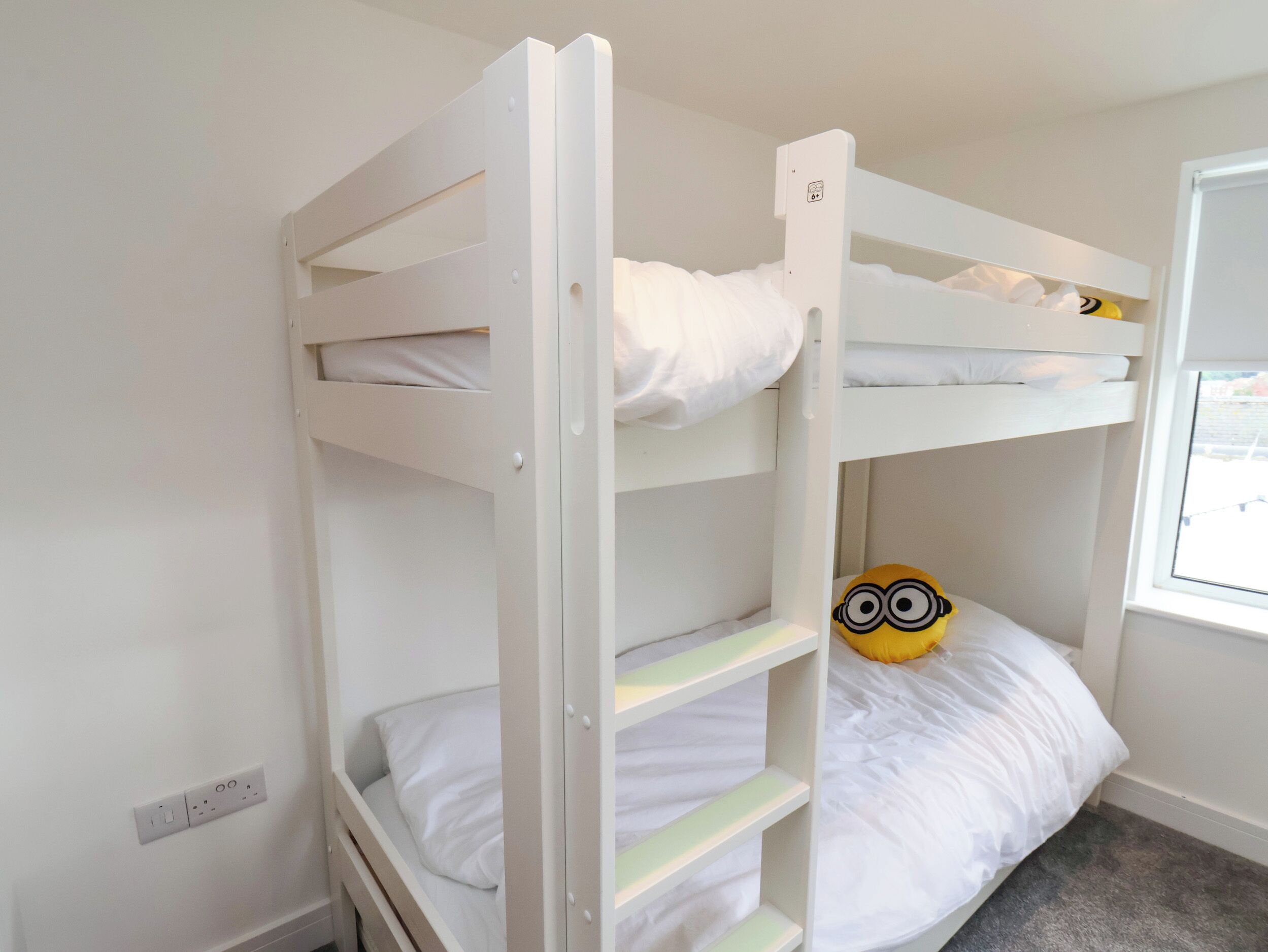 Una cama litera con ropa blanca y un peluche de Minion en la cama superior.