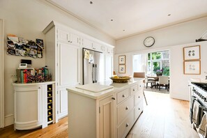 A modern kitchen with white cabinetry, a central island, and a dining area with natural light. - A Timeless Family Home (London)