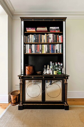 A bookshelf with a variety of books and a selection of bottles on a wooden console table. - A Timeless Family Home (London)