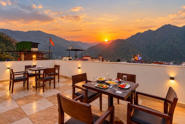A rooftop dining area with a view of the sunset and mountains.