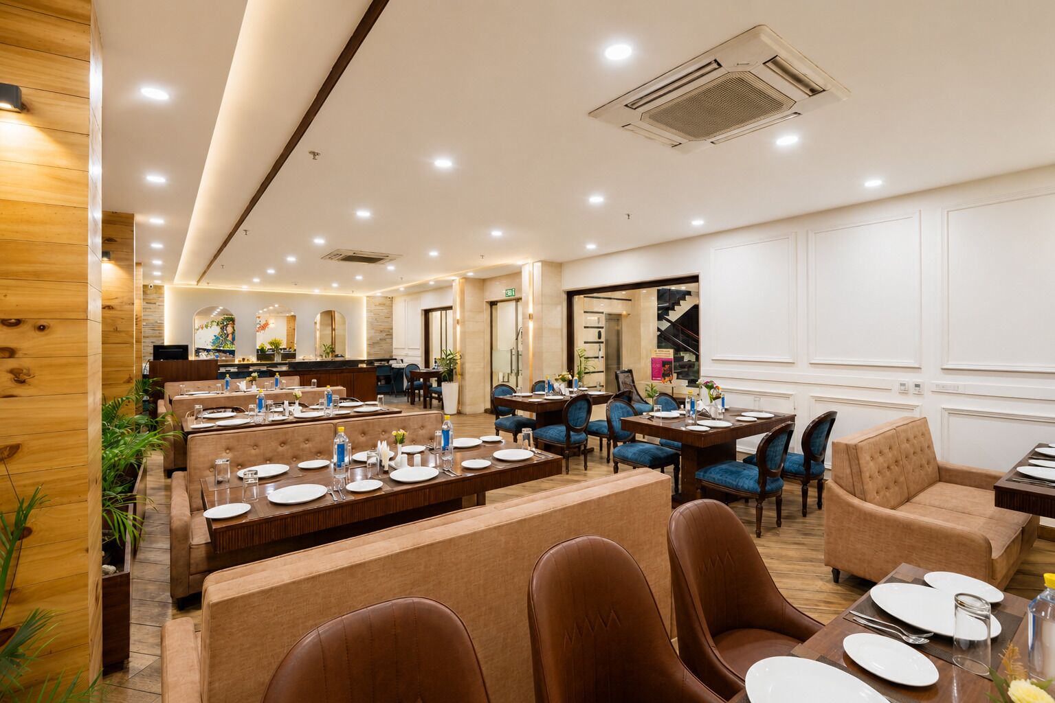A hotel dining area with multiple tables and chairs, a reception desk, and a staircase leading to an upper floor.