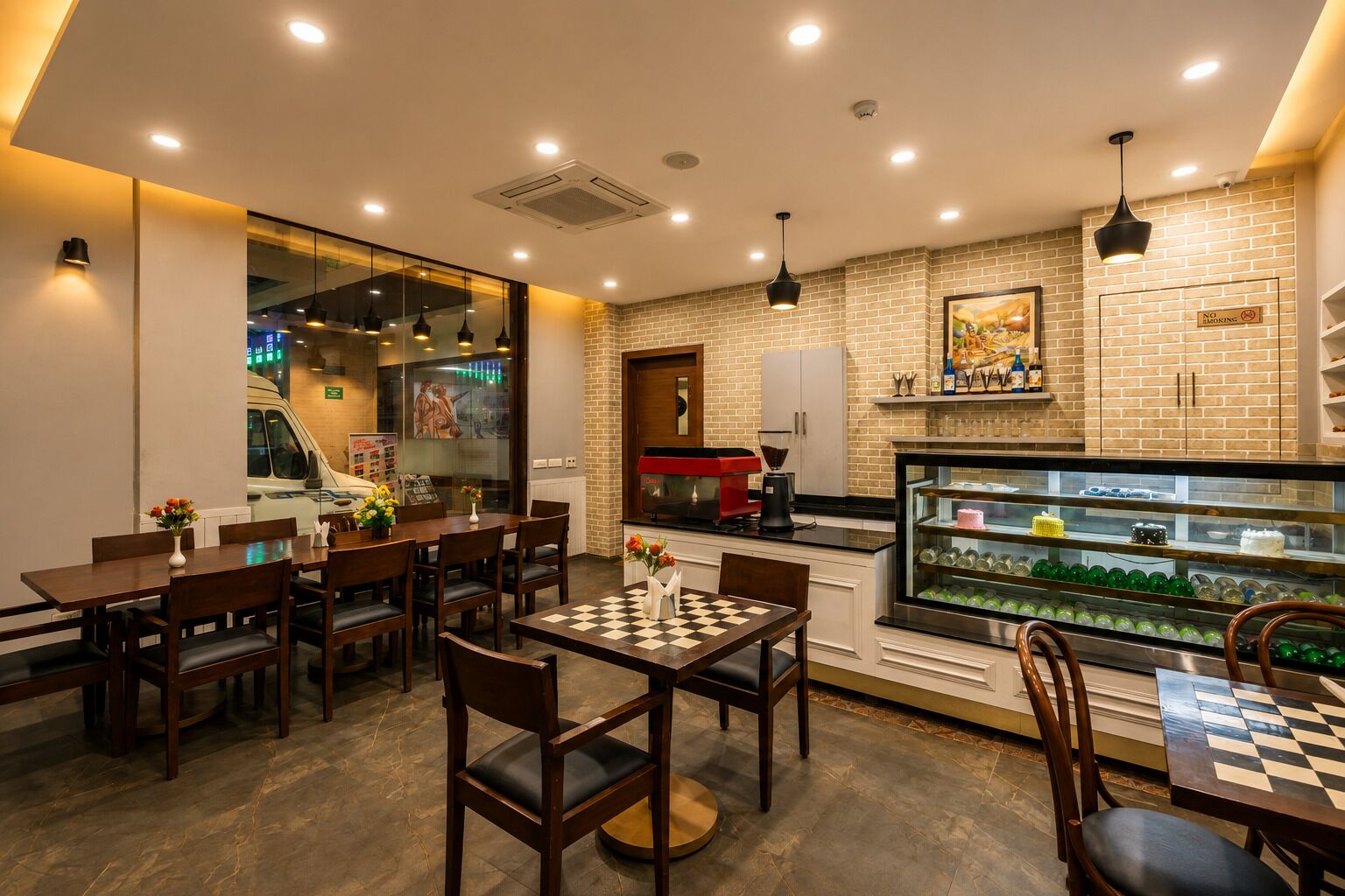 A restaurant interior with wooden tables and chairs, a coffee machine, a display case with desserts, and a brick wall.
