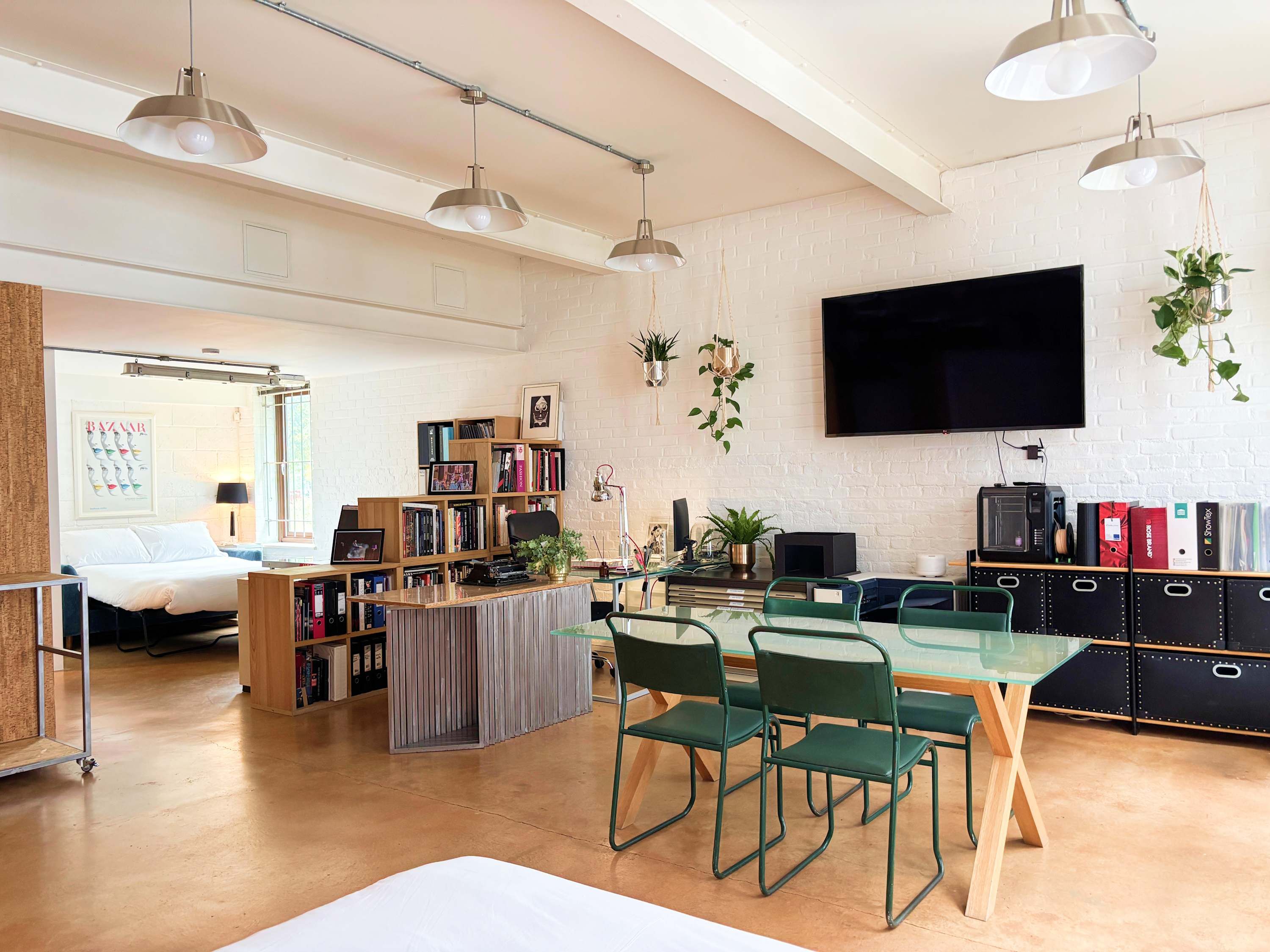 A modern living room with a dining area, a flat-screen TV mounted on the wall, and a bookshelf filled with books and decorative items.