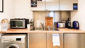 Uma cozinha compacta com máquina de lavar, torradeira, chaleira e cafeteira.