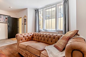 Ein Zimmer mit einem braunen Ledersofa, einem gemusterten Sitzkissen und einem Fenster mit Vorhängen.