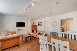 A modern living room with a flat-screen TV, leather sofas, a dining table with chairs, and a kitchen area in the background. - Host & Stay | Regency Courtyard (Brighton and Hove)