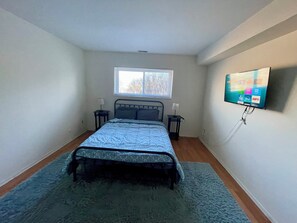 Ein Schlafzimmer mit einem Bett, einem Fenster, zwei Nachttischen und einem an der Wand befestigten Fernseher.