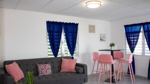Ein modernes Wohnzimmer mit einem grauen Sofa, rosafarbenen Sesseln und blauen Vorhängen.