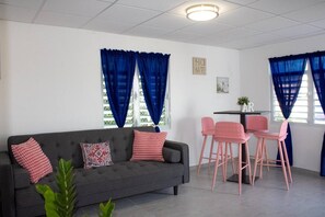 Ein modernes Wohnzimmer mit einem grauen Sofa, rosafarbenen Sesseln und blauen Vorhängen.