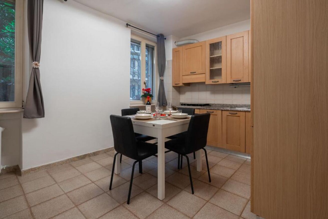 Una piccola cucina con un tavolo da pranzo per due persone, pensili in legno e una finestra con tenda.
