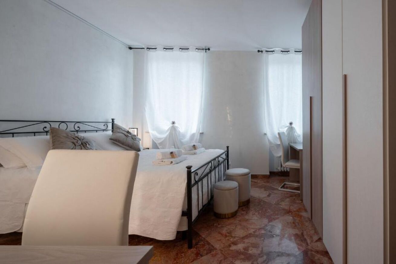 A bedroom with a bed, two bedside tables, a chair, a mirror, and a window with curtains.