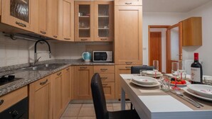 A kitchen with wooden cabinets, a microwave, a sink, and a dining area set for a meal. - Charming Dorsoduro Venice Stay Near Art Museums and Canals (Venezia VE, Italy)