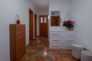 Ein Flur mit einem Holzschrank, einer weißen Kommode mit Schubladen, einem Spiegel und einem Blumentopf.
