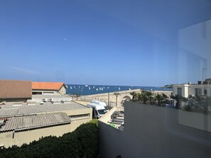 A coastal view with buildings, a clear sky, and sailboats on the water. - (026) Le côté Remparts (Antibes)