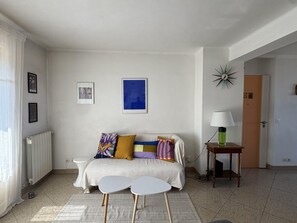 A living room with a sofa, two side tables, a lamp, and a radiator. - (026) Le côté Remparts (Antibes)