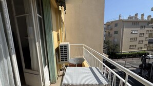 Een balkon met een tafel en stoelen met ruitpatroon, een airconditioning en een uitzicht op een stadsgezicht met gebouwen.