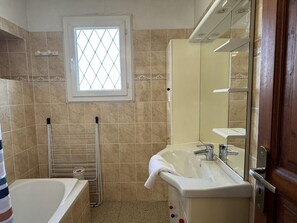 Et badeværelse med badekar, vask, spejl og et vindue.
