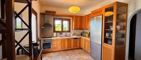 A kitchen with wooden cabinets, a stainless steel refrigerator, and a window with a view of greenery.