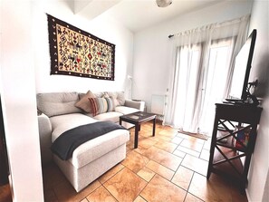 A living room with a sofa, a coffee table, a radiator, and a bookshelf. - 3-bedroom house in perfect Makry Gialos with AC for relaxing stays (Makry Gialos)