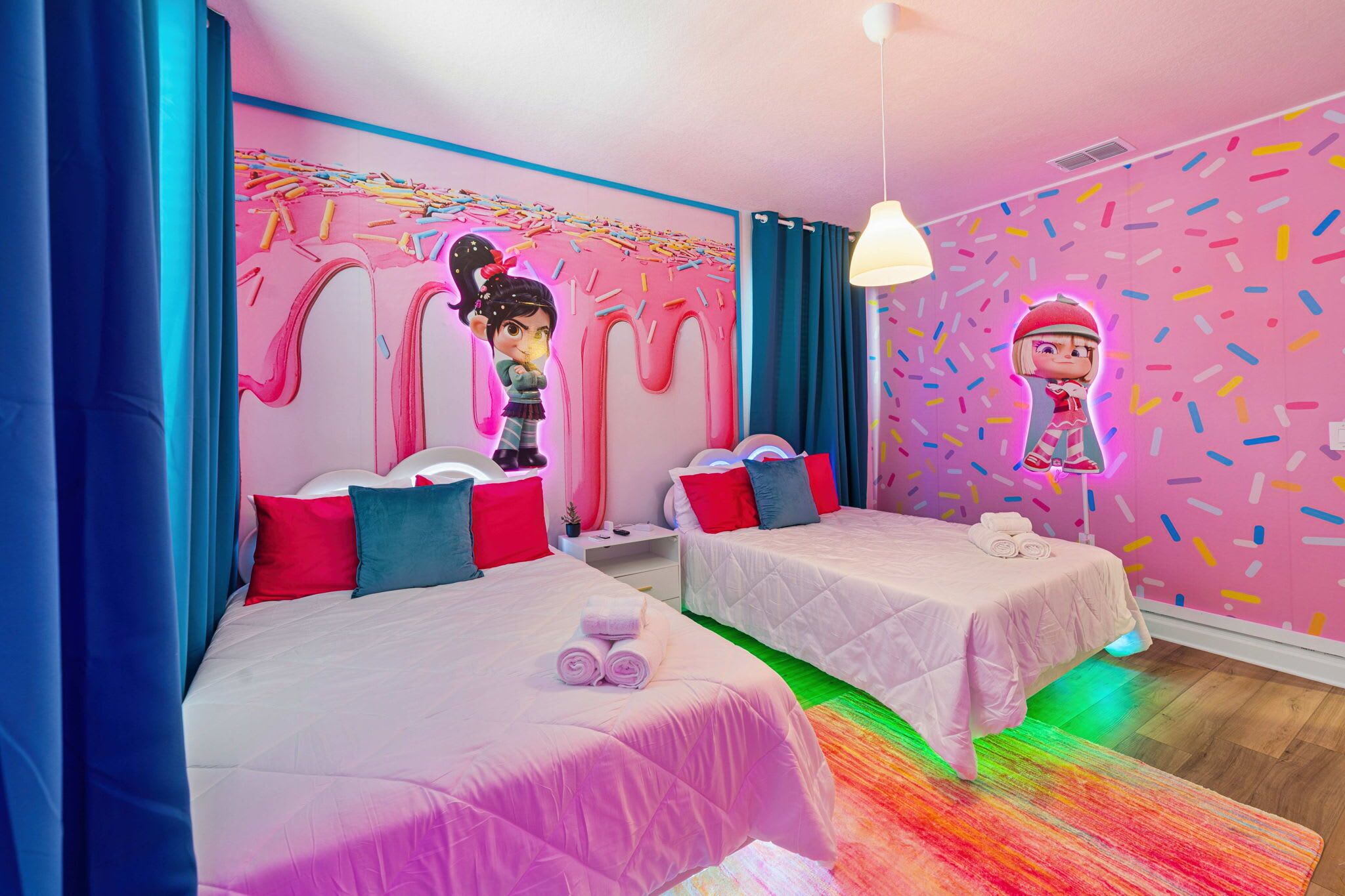 Une chambre d’hôtel avec deux lits, des rideaux aux couleurs vives, une fresque murale éclatante et un tapis coloré.