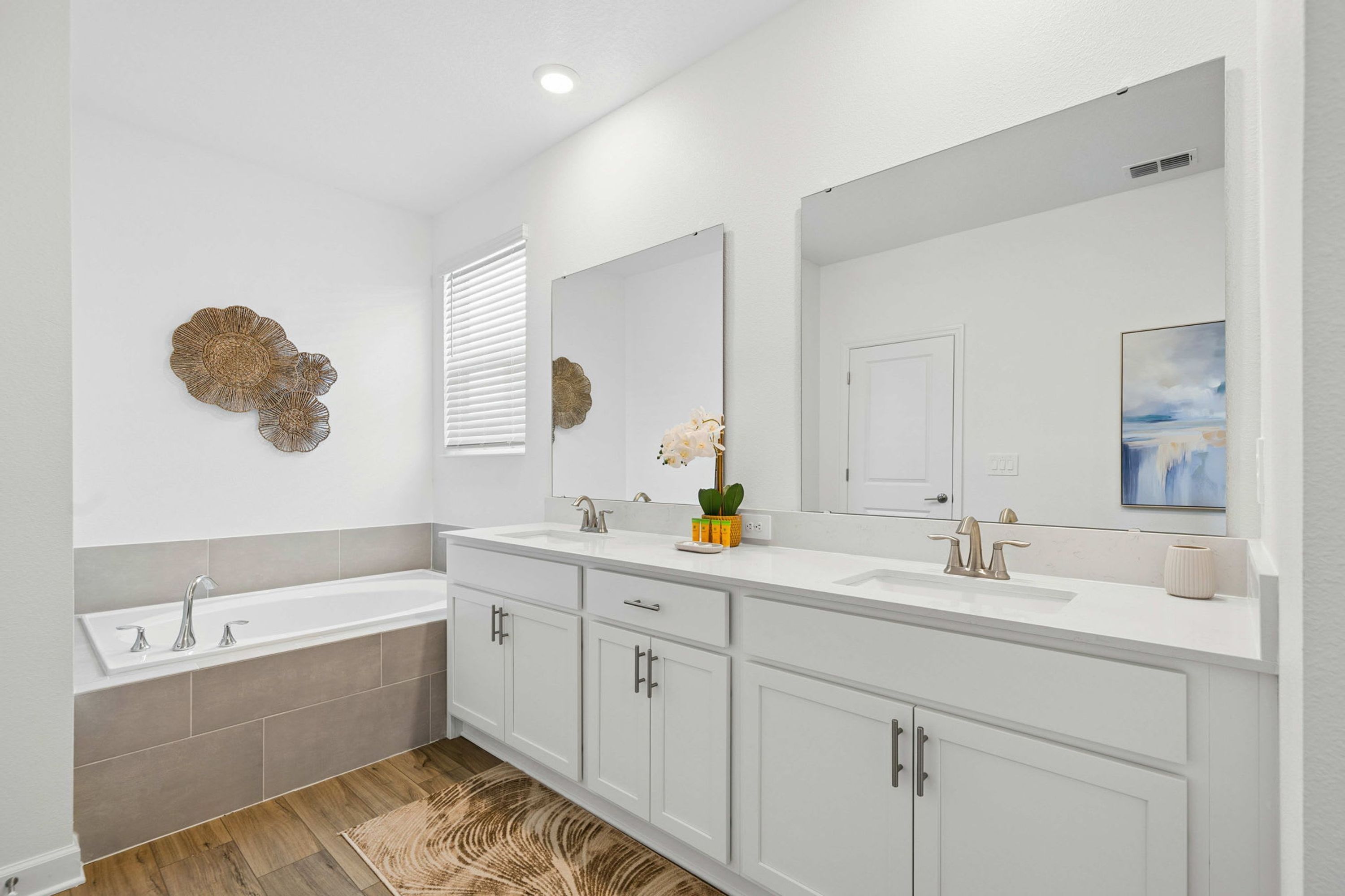 A modern bathroom with a double sink vanity, a bathtub, and a large mirror.
