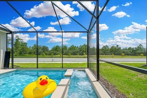 A swimming pool with a duck float, surrounded by a covered area with a view of a road and trees. - Brand New 5BR 5BA Villa w Pool Spa Game Room 7800 (Kissimmee)