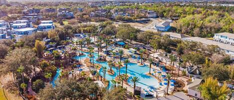 Eine Vogelperspektive zeigt ein Resort mit mehreren Schwimmbecken, Palmen und verschiedenen Gebäuden.