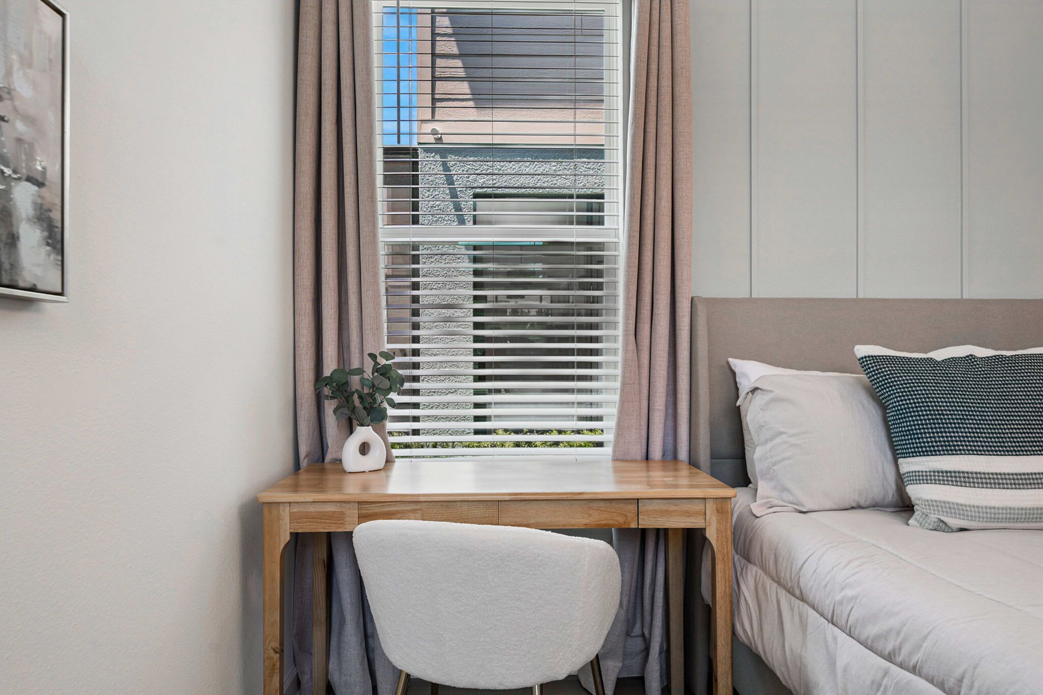 A bedroom with a bed, a desk with a chair, and a window with blinds.