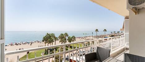 A balcony with wicker furniture, a bottle of champagne, and a view of a beach with palm trees and umbrellas.