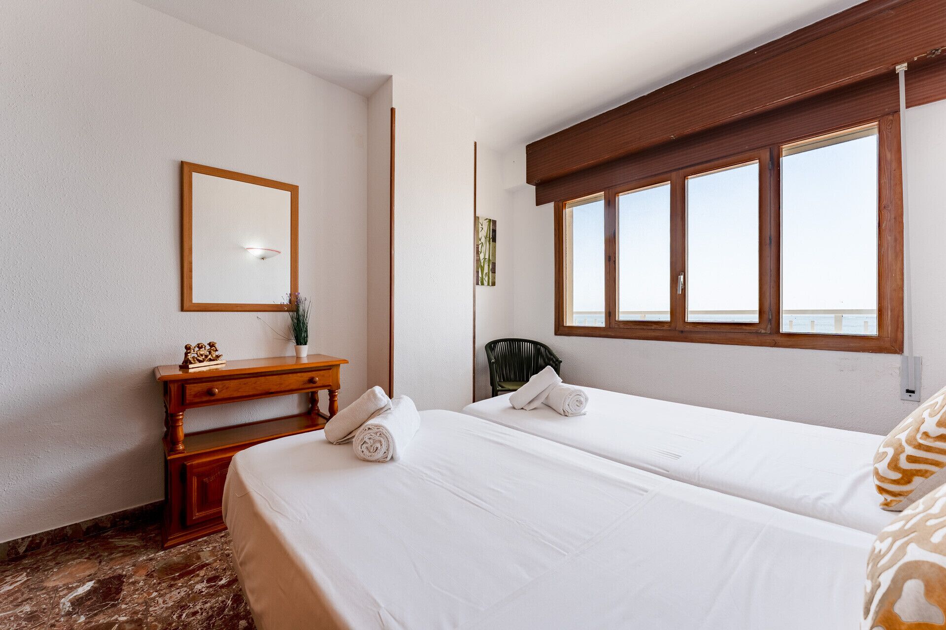 Een hotelkamer met twee bedden, een houten dressoir, een spiegel en een raam met uitzicht.