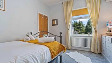 A bedroom with a bed, a dresser, a window with curtains, a radiator, and a small rug.