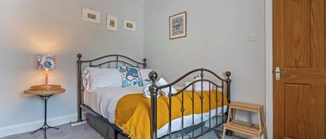 A bedroom with a bed, a bedside table, a small stool, and a door.