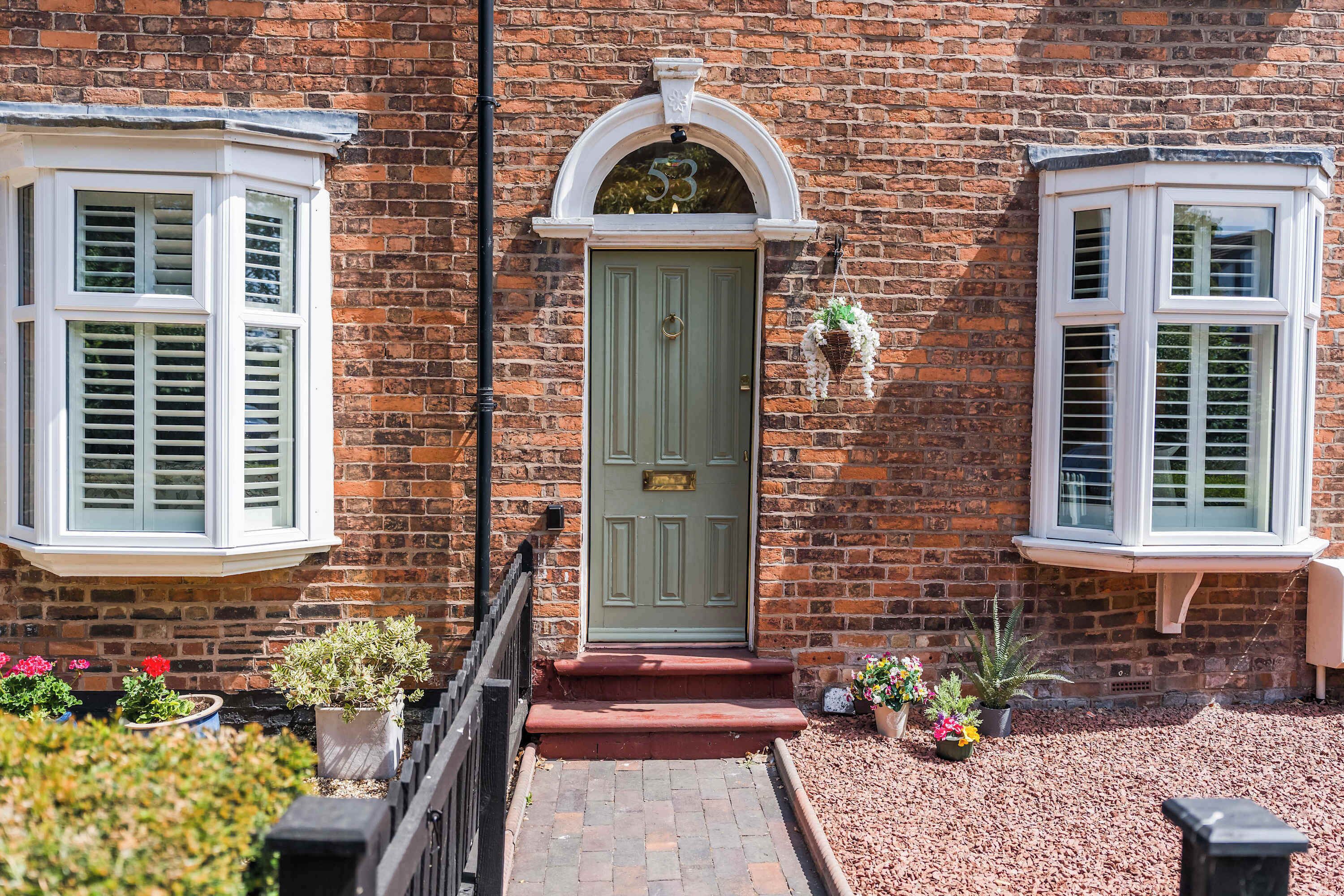 A brick house with a green door, white window frames, and a small porch with steps leading to the entrance.
