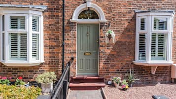A brick house with a green door, white window frames, and a small porch with steps leading to the entrance.