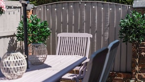 Eine Terrasse im Freien mit einem Holztisch und -stühlen, umgeben von einem Holzzaun und Topfpflanzen.