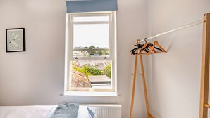Une chambre avec un lit, une fenêtre donnant sur un paysage agréable, un radiateur et un étendoir.