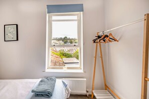 Ein Schlafzimmer mit einem Bett, einem Fenster mit Blick, einem Heizkörper und einem Wäscheständer.