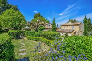 A traditional stone building with a tiled roof, surrounded by lush greenery and a well-maintained garden with a stone pathway. - Mas Les Cigales in Saint-r My-de-provence (St.-Rémy-de-Provence)