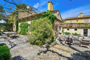 A courtyard with stone flooring, outdoor furniture, and a large tree. - Mas Les Cigales in Saint-r My-de-provence (St.-Rémy-de-Provence)