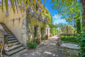 A courtyard with a stone staircase, a metal table and chairs, and large vases. - Mas Les Cigales in Saint-r My-de-provence (St.-Rémy-de-Provence)