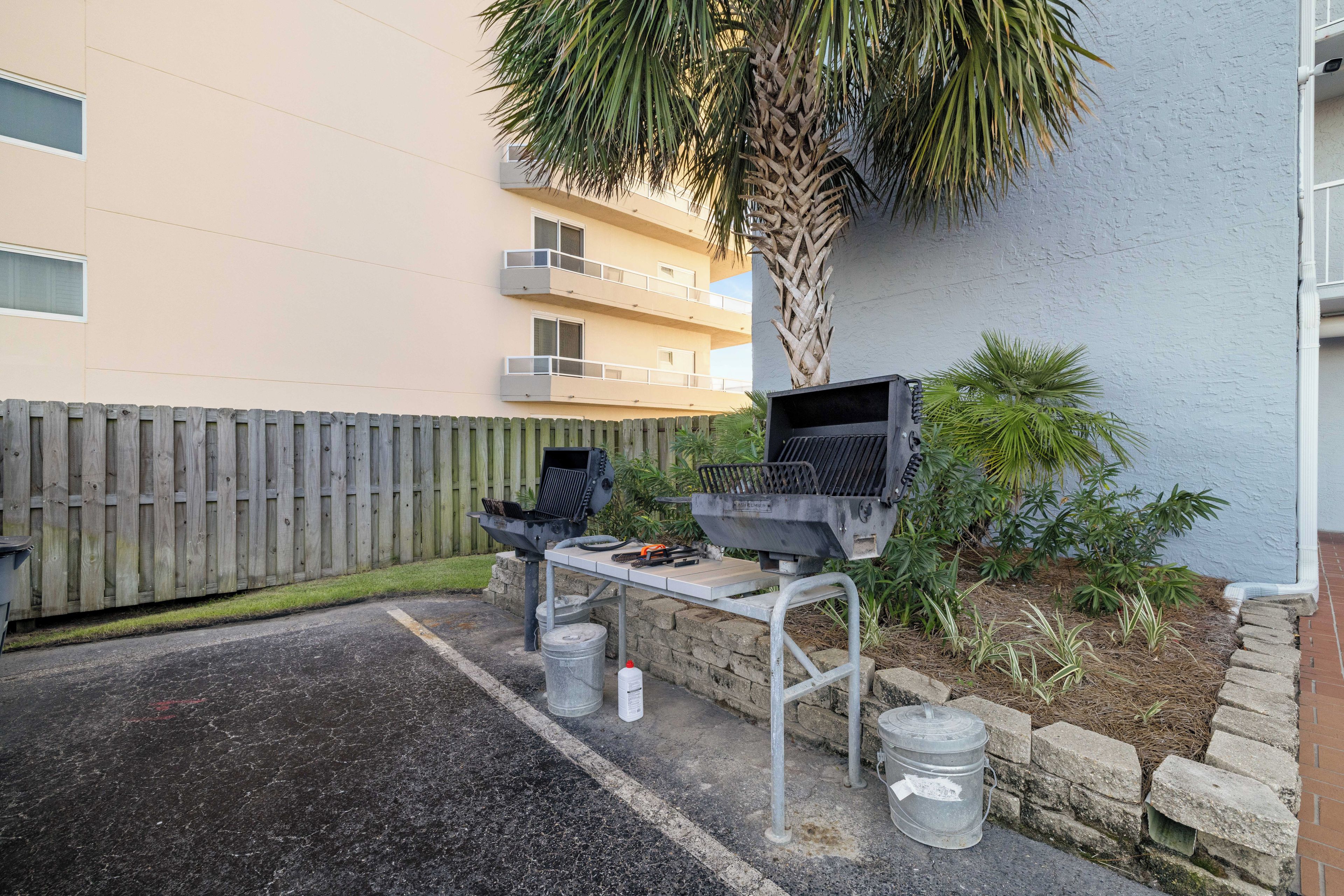 En utomhusplats för grillning med en grill och ett bord, ett trästaket och en byggnad i bakgrunden.