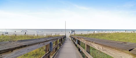 Een houten looppad dat naar een strand leidt, onder een heldere lucht.